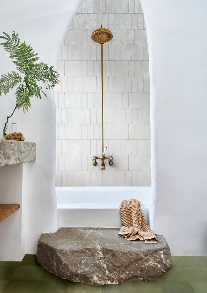 Beige subway tiles laid in vertical offset pattern inside an arched shower with brass shower fittings and stone step