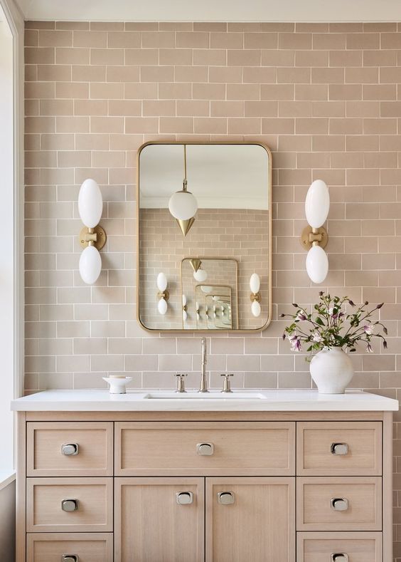 Bathroom vanity with natural oak drawers and beige subway tiles laid in a traditional brick bond pattern, styled with rounded mirror and white wall sconces