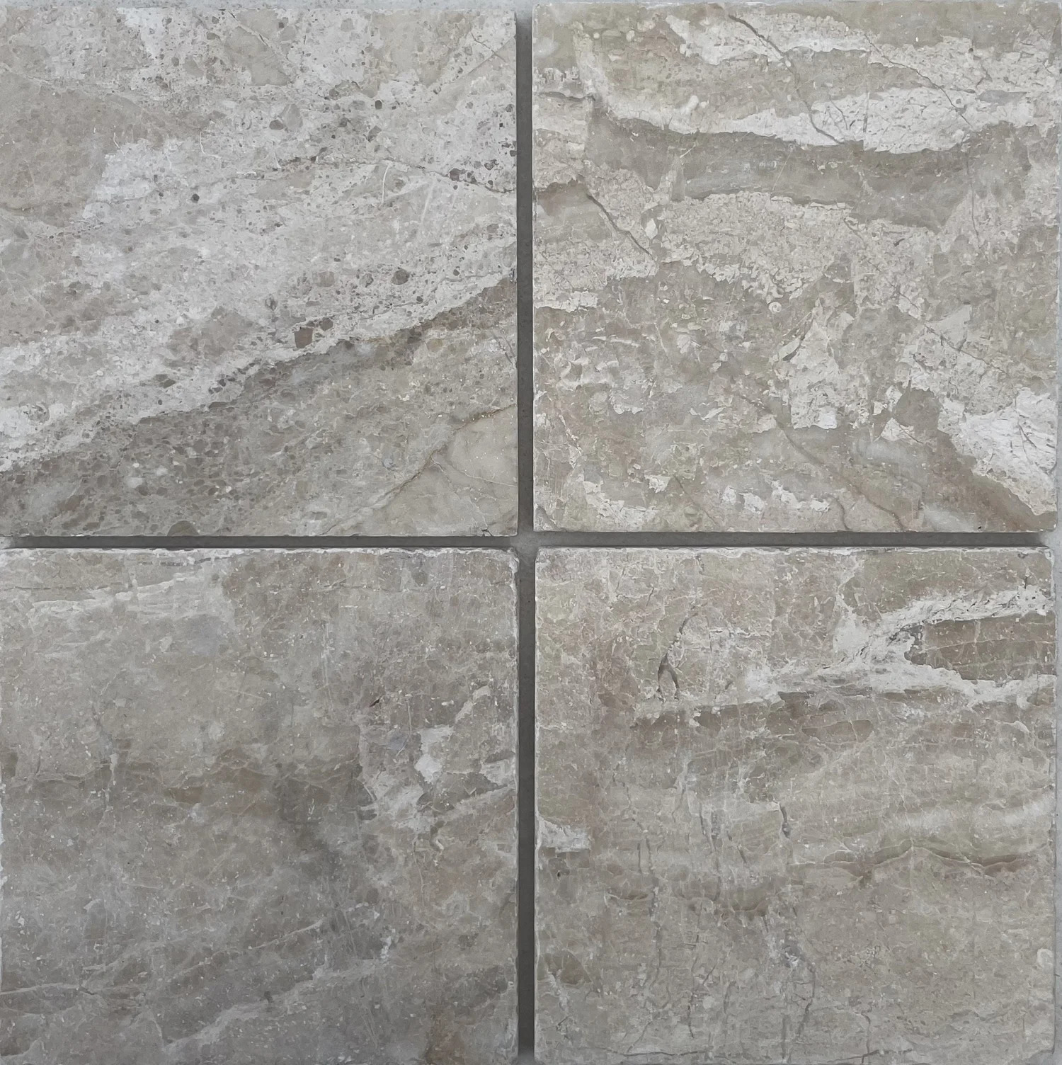 Tumbled square natural stone tiles in mixed neutral tones, laid in a soft grid across an outdoor floor. Visible variation and softened edges.