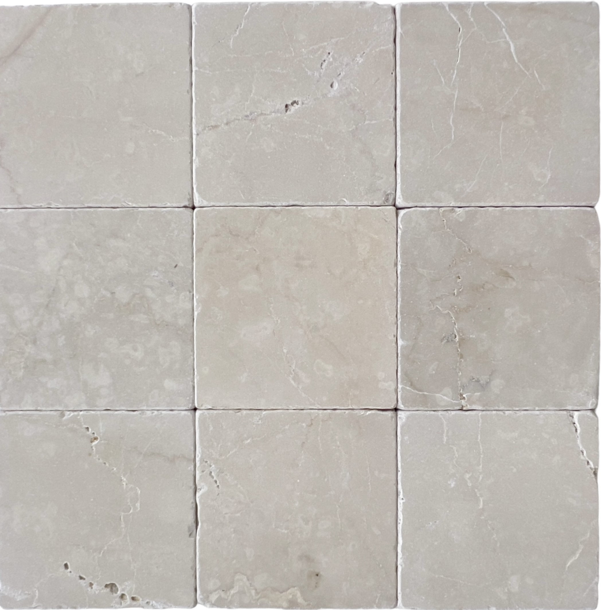 Tumbled square natural stone tiles in mixed neutral tones, laid in a soft grid across an outdoor floor. Visible variation and softened edges.