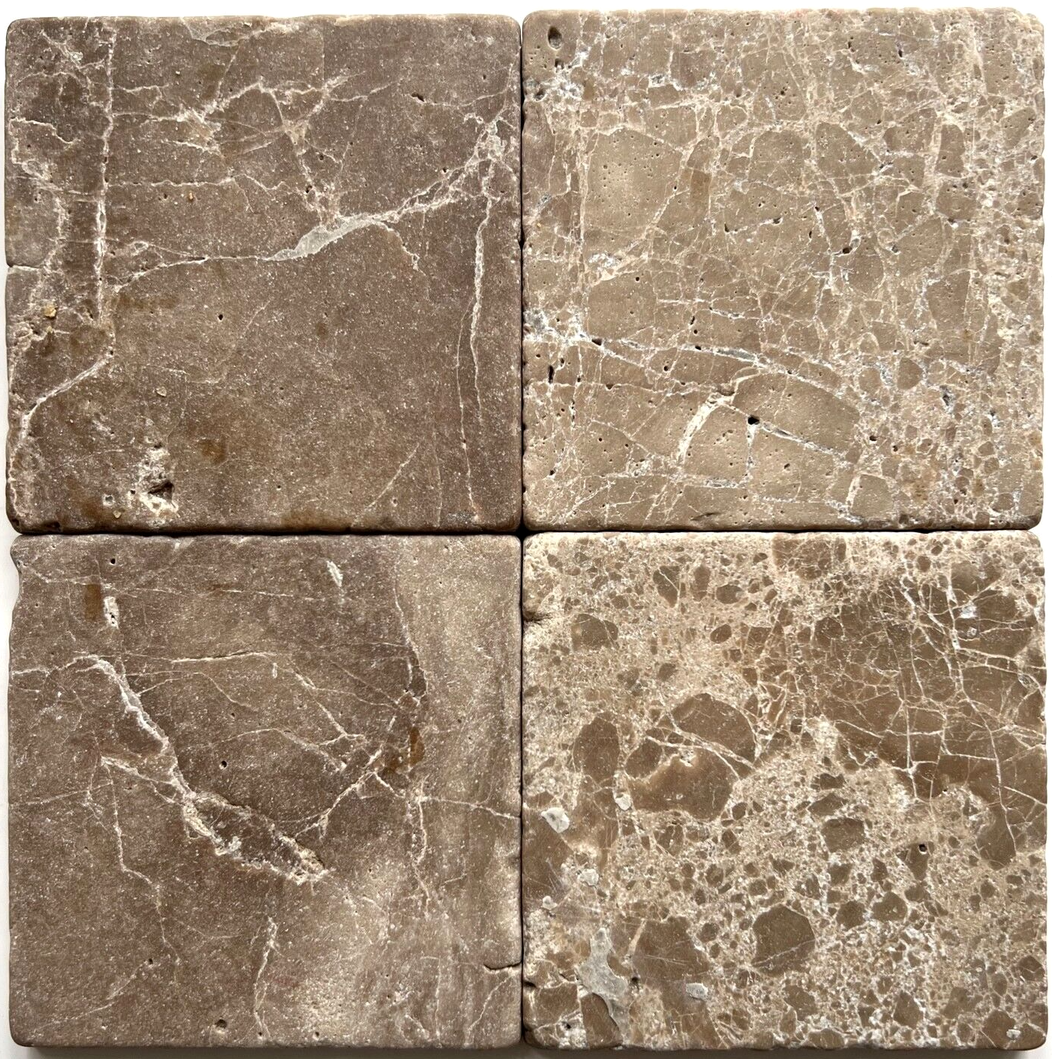 Tumbled square natural stone tiles in mixed neutral tones, laid in a soft grid across an outdoor floor. Visible variation and softened edges.