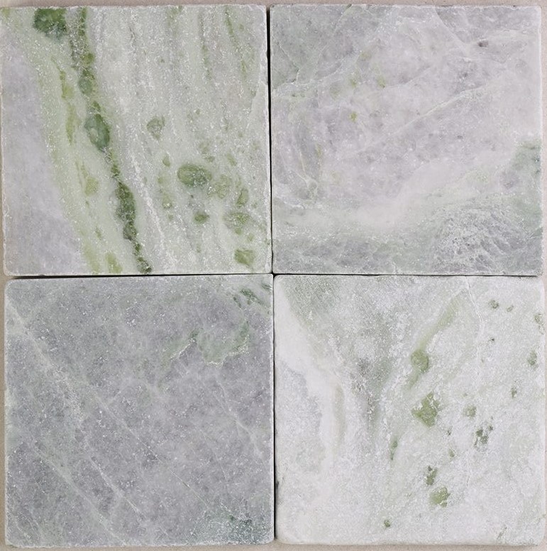 Tumbled square natural stone tiles in mixed neutral tones, laid in a soft grid across an outdoor floor. Visible variation and softened edges.