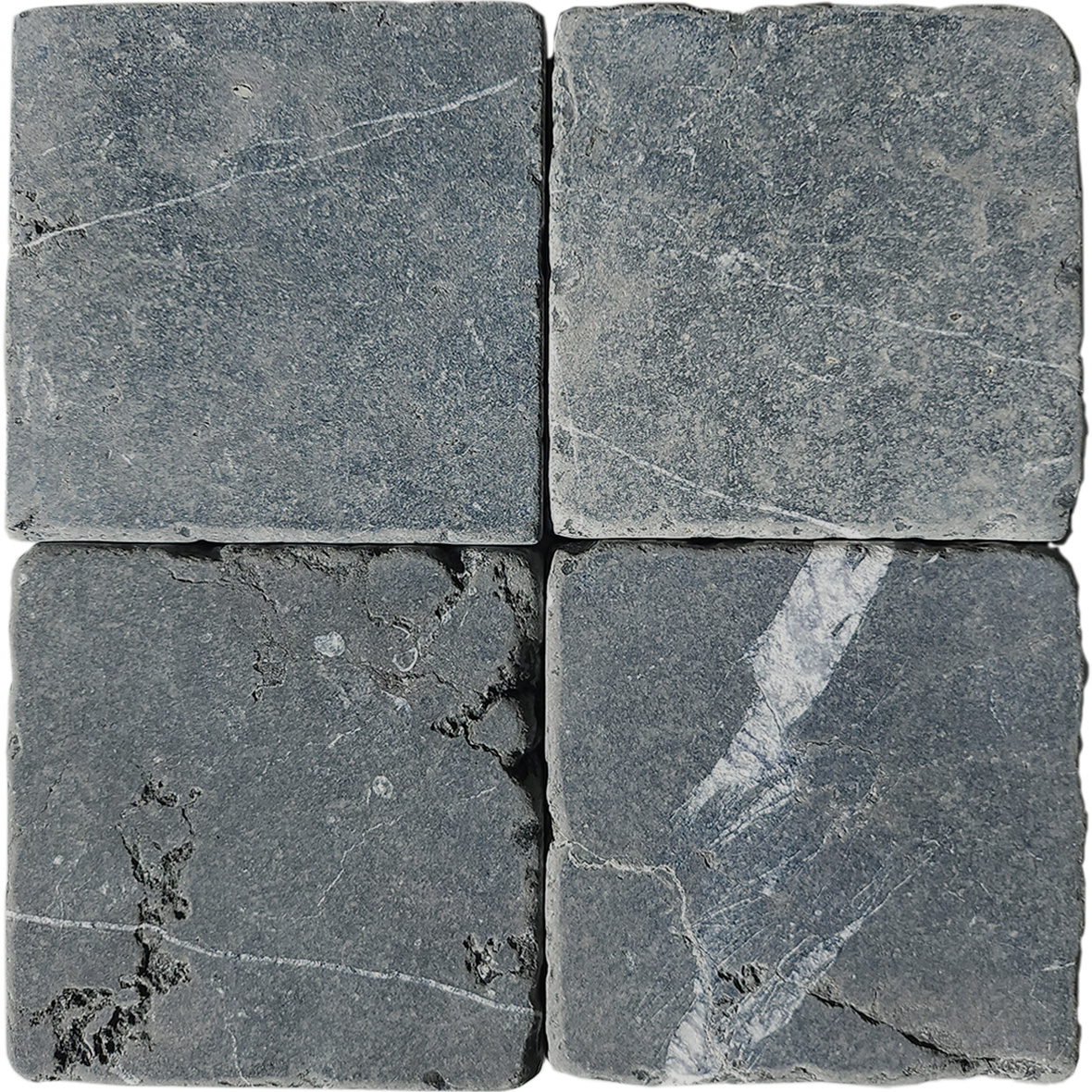 Tumbled square natural stone tiles in mixed neutral tones, laid in a soft grid across an outdoor floor. Visible variation and softened edges.