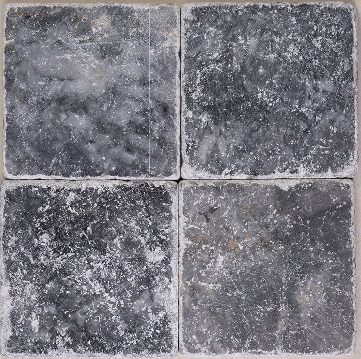 Tumbled square natural stone tiles in mixed neutral tones, laid in a soft grid across an outdoor floor. Visible variation and softened edges.