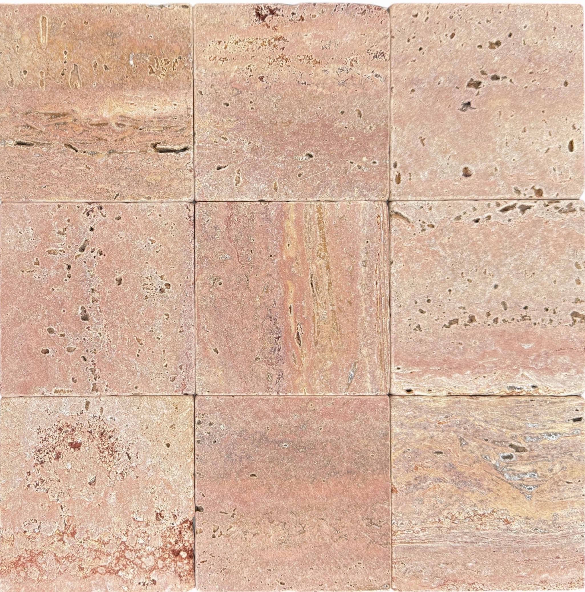 Tumbled square natural stone tiles in mixed neutral tones, laid in a soft grid across an outdoor floor. Visible variation and softened edges.