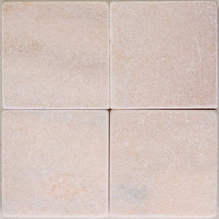 Tumbled square natural stone tiles in mixed neutral tones, laid in a soft grid across an outdoor floor. Visible variation and softened edges.