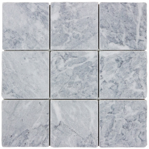 Tumbled square natural stone tiles in mixed neutral tones, laid in a soft grid across an outdoor floor. Visible variation and softened edges.